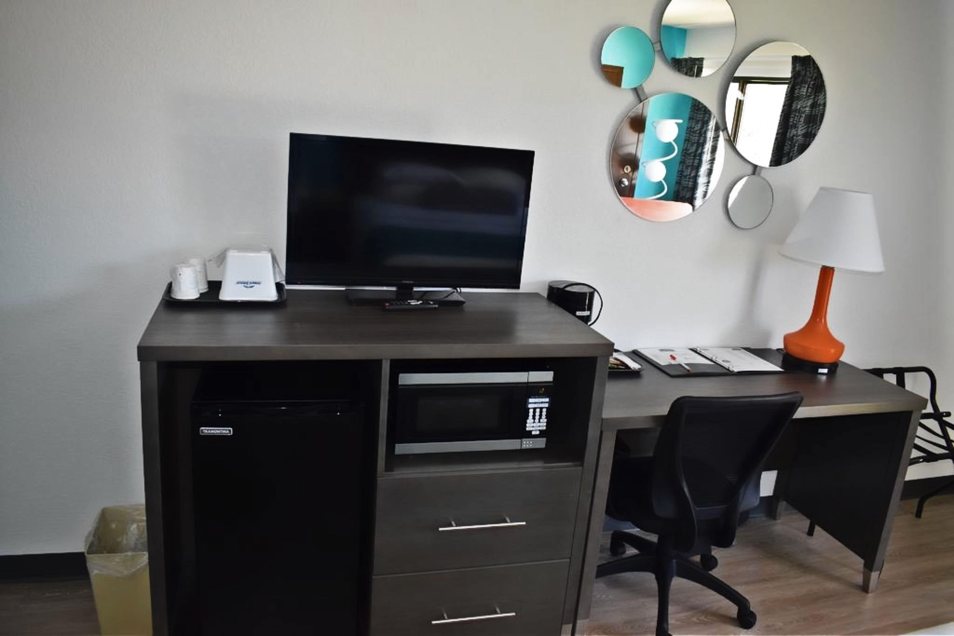 Un espacio de oficina moderno con un escritorio, computadora e impresora. Hay varios espejos en la pared y una lámpara en el escritorio.