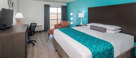 Una habitación de hotel con cama, escritorio con computadora, silla y ventana con cortinas.