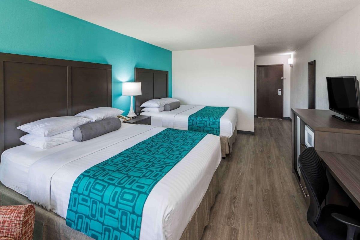 A hotel room with two beds, a desk, a TV, and a door.
