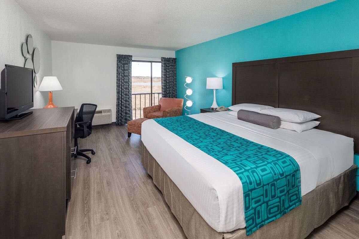 A hotel room with a bed, a desk with a computer, a chair, a TV, and a window with curtains.