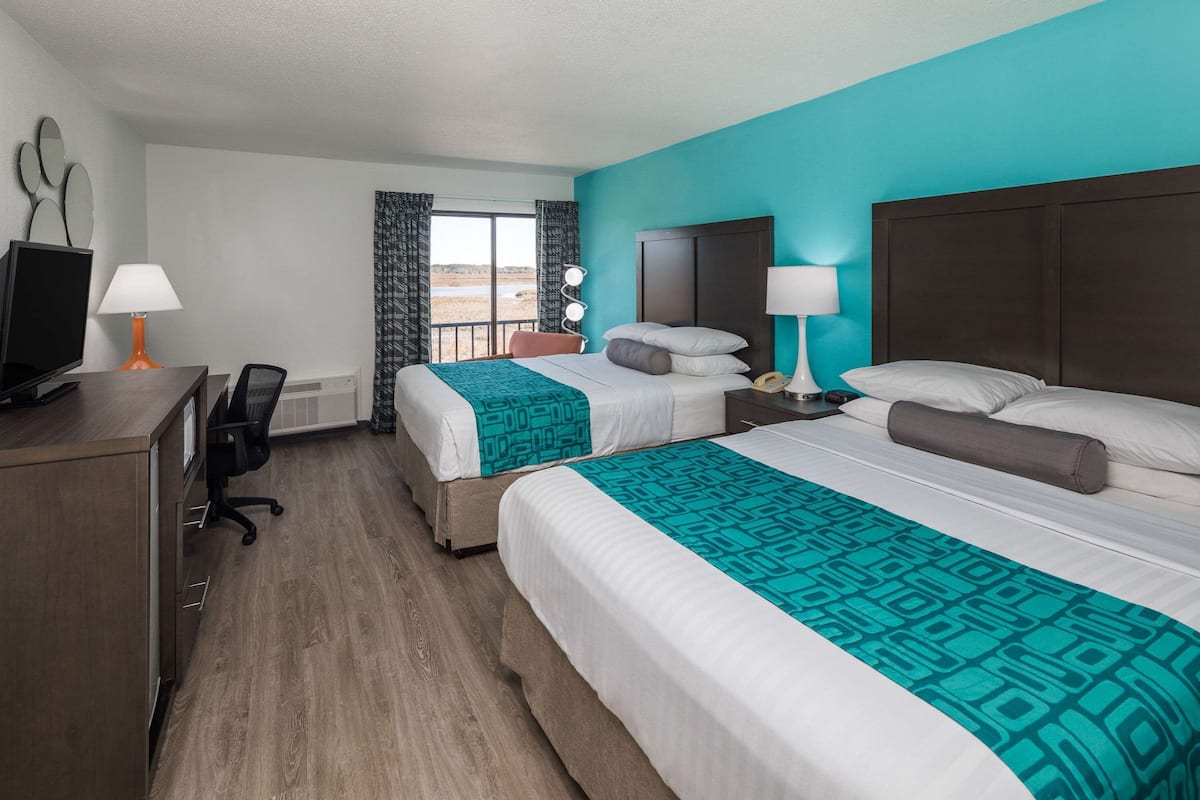 A hotel room with two beds, a desk with a computer, and a window with curtains.