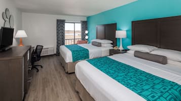 A hotel room with two beds, a desk with a computer, and a window with curtains.