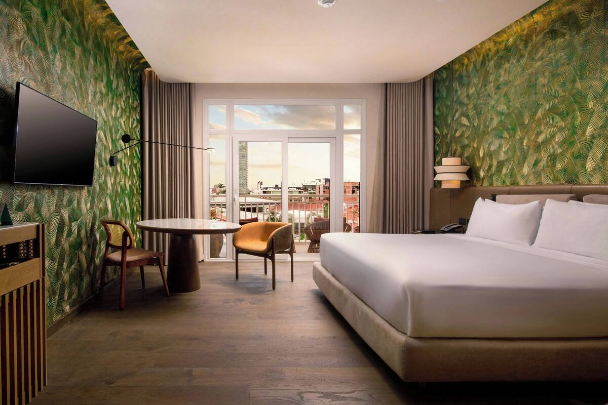 A hotel room with a bed, a TV, a dining table, and chairs.