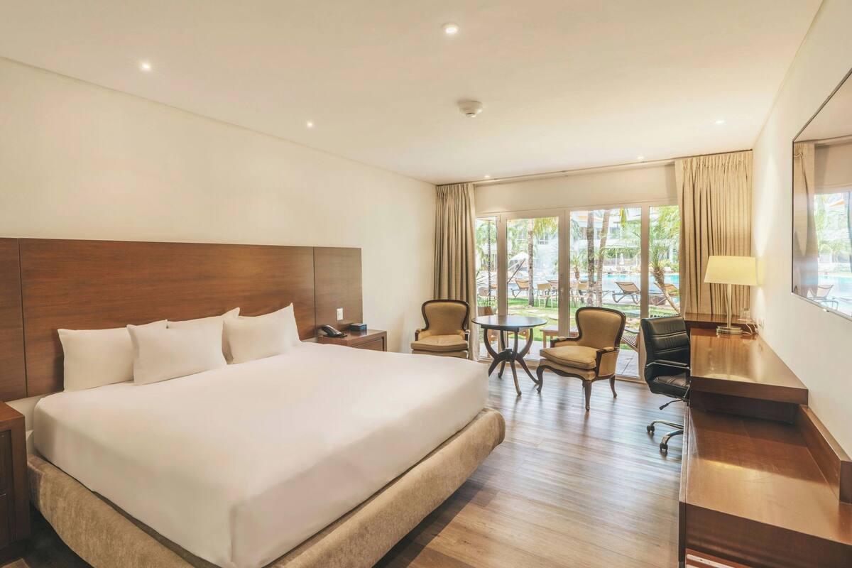 A hotel room with a large bed, a desk, a chair, and a view of the outdoors.