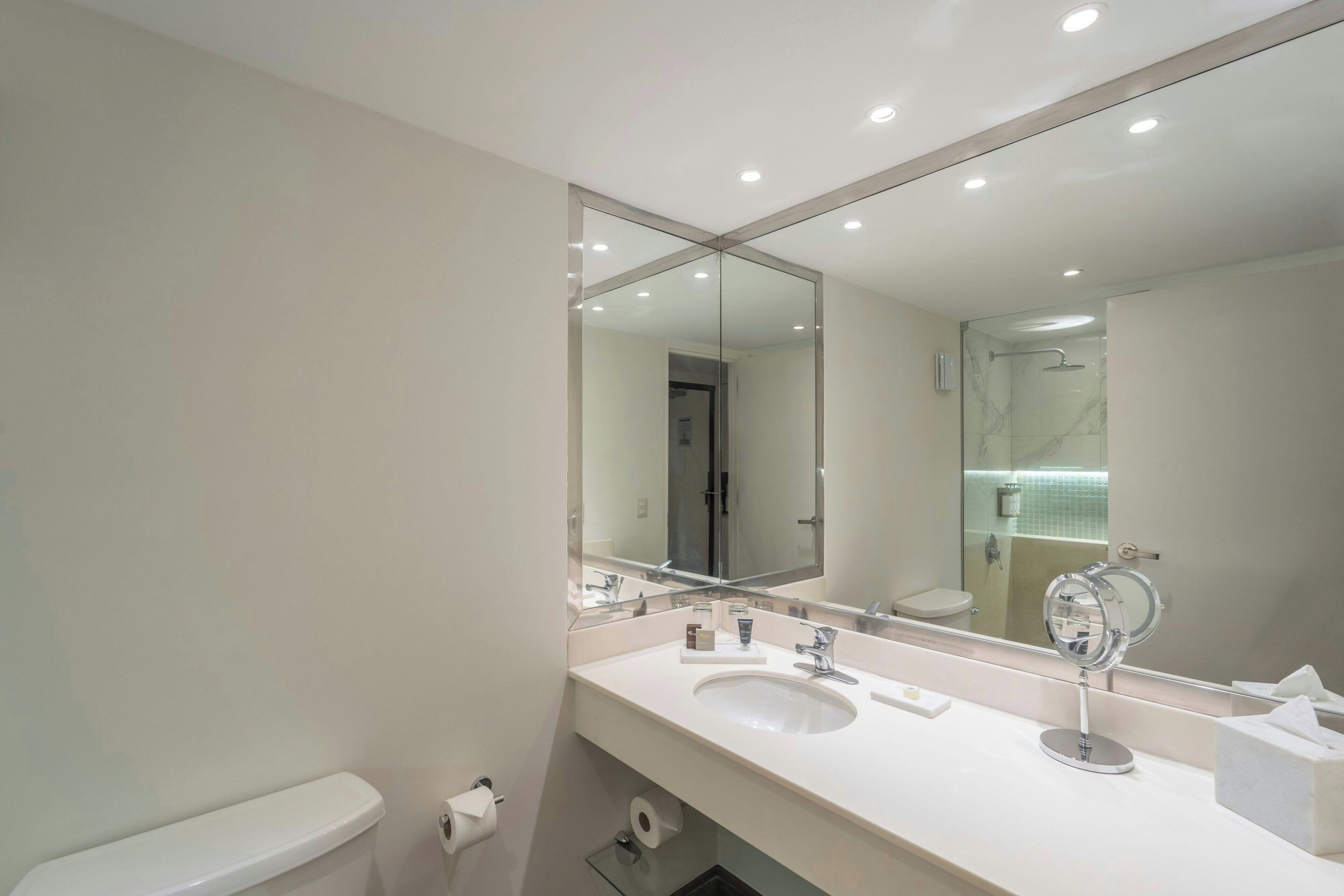 A modern bathroom with a large mirror, white sink, and a toilet.
