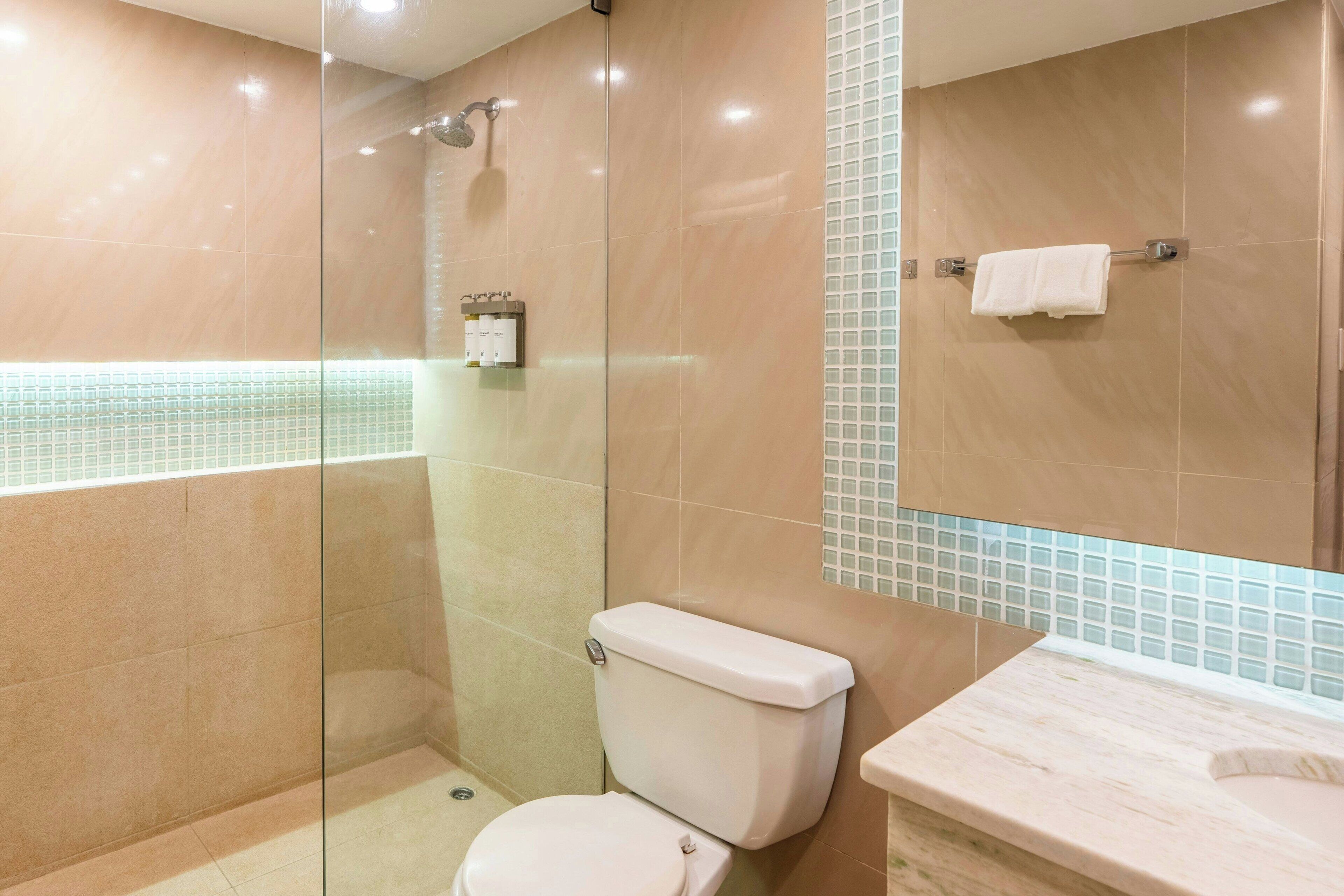 Ein modernes Badezimmer mit einer gläsernen Duschkabine, einer Toilette und einem Waschbecken mit Marmorplatte.