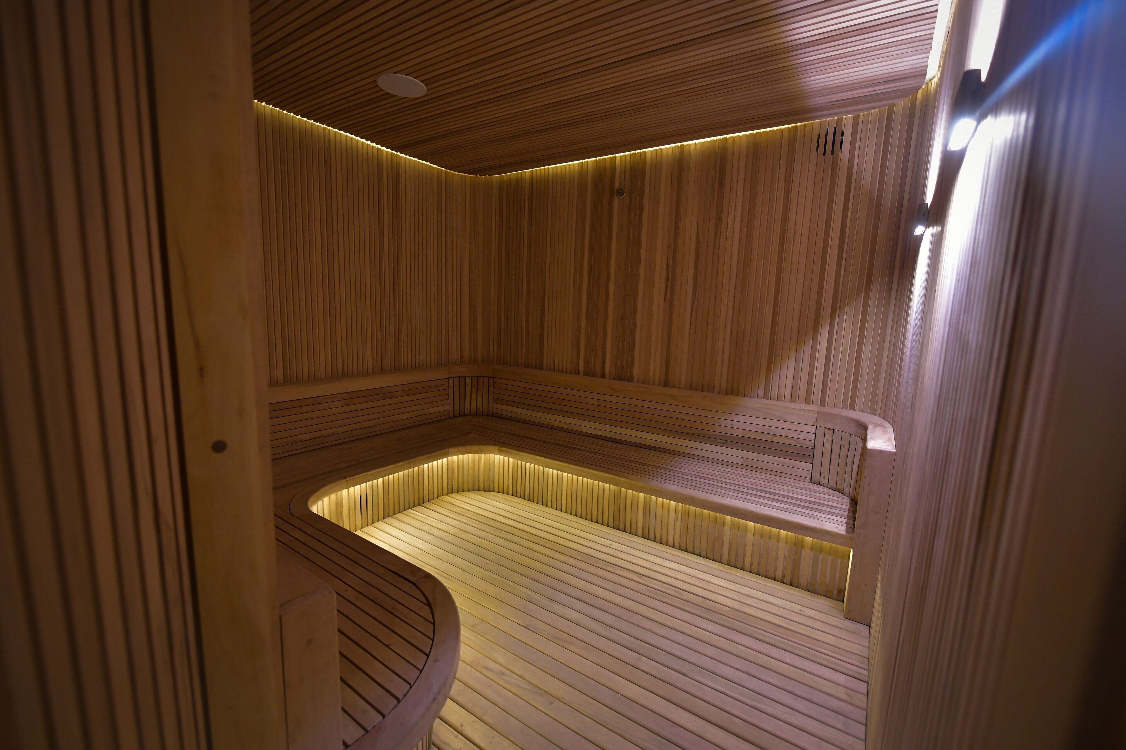 Una sauna con paredes y bancos de madera, un suelo inclinado e iluminación empotrada en el techo.