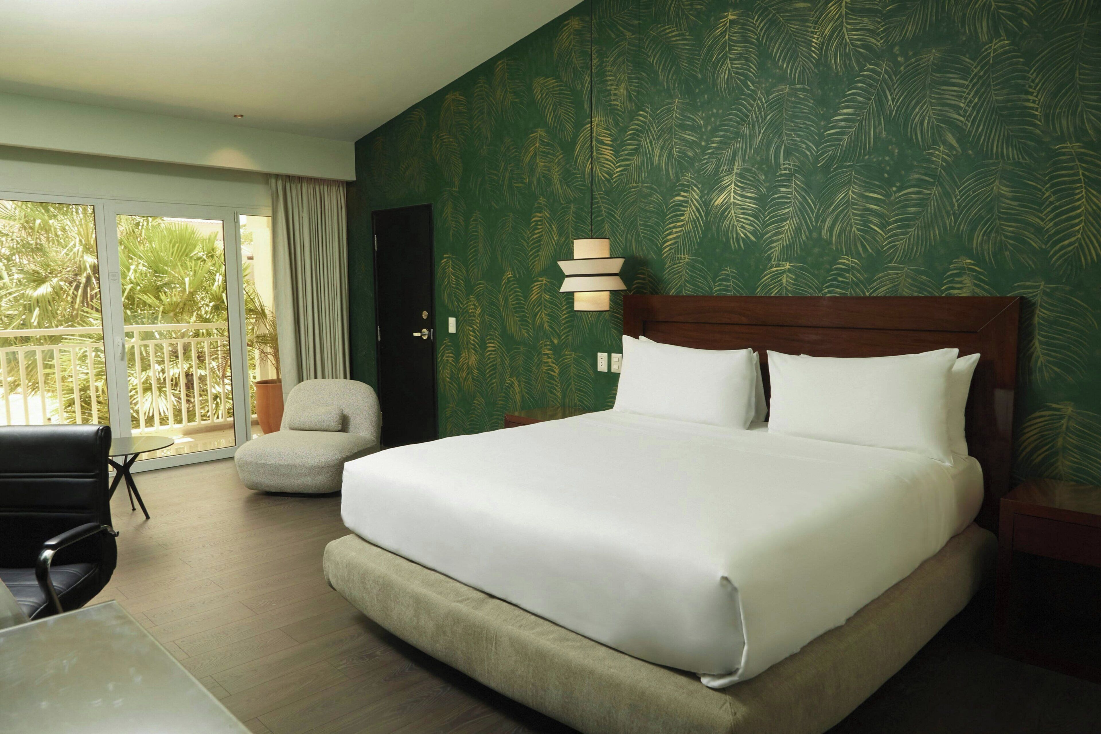 A hotel room with a large bed, a chair, a table, and a view of the outdoors.