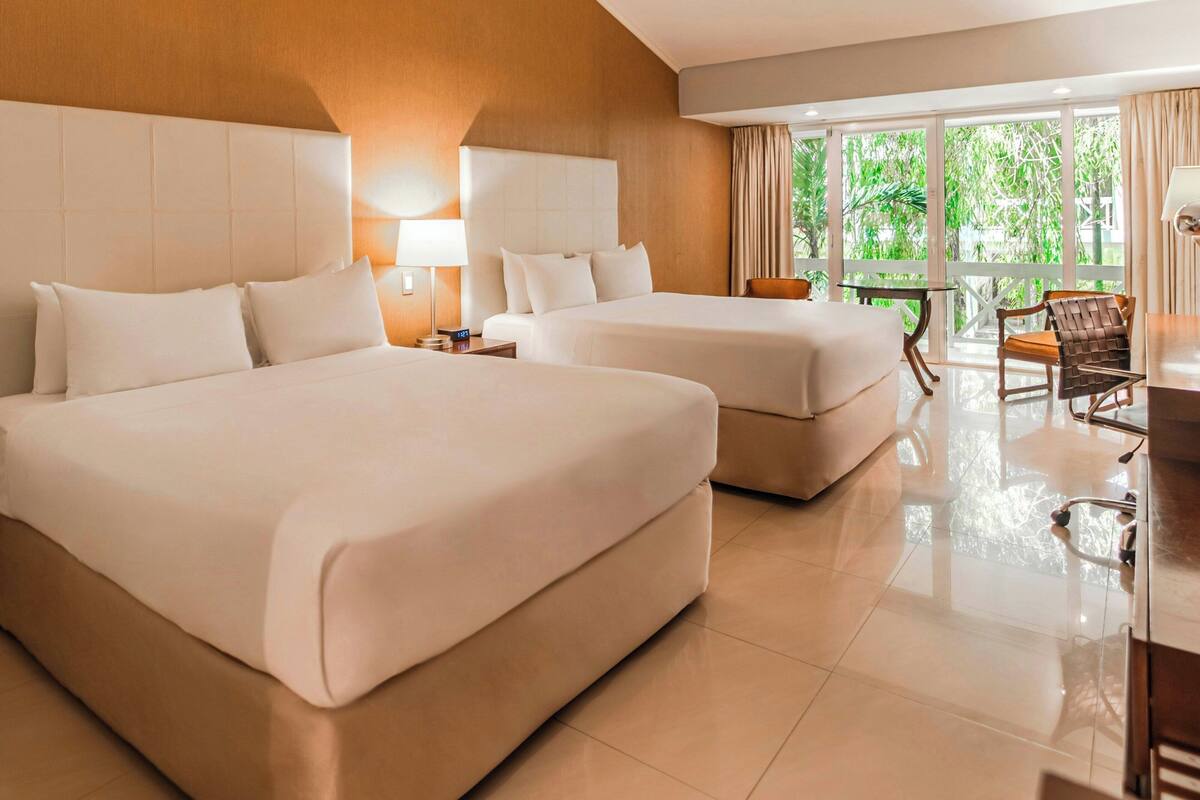 A hotel room with two large beds, a desk, and a chair.