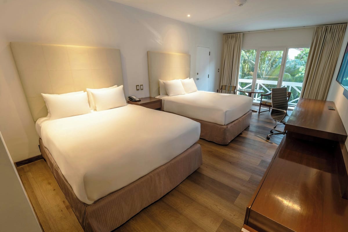 A hotel room with two beds, a desk, and a balcony with a chair.