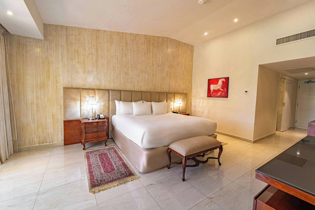 A spacious bedroom with a large bed, bedside tables, a bench, and a red artwork on the wall.