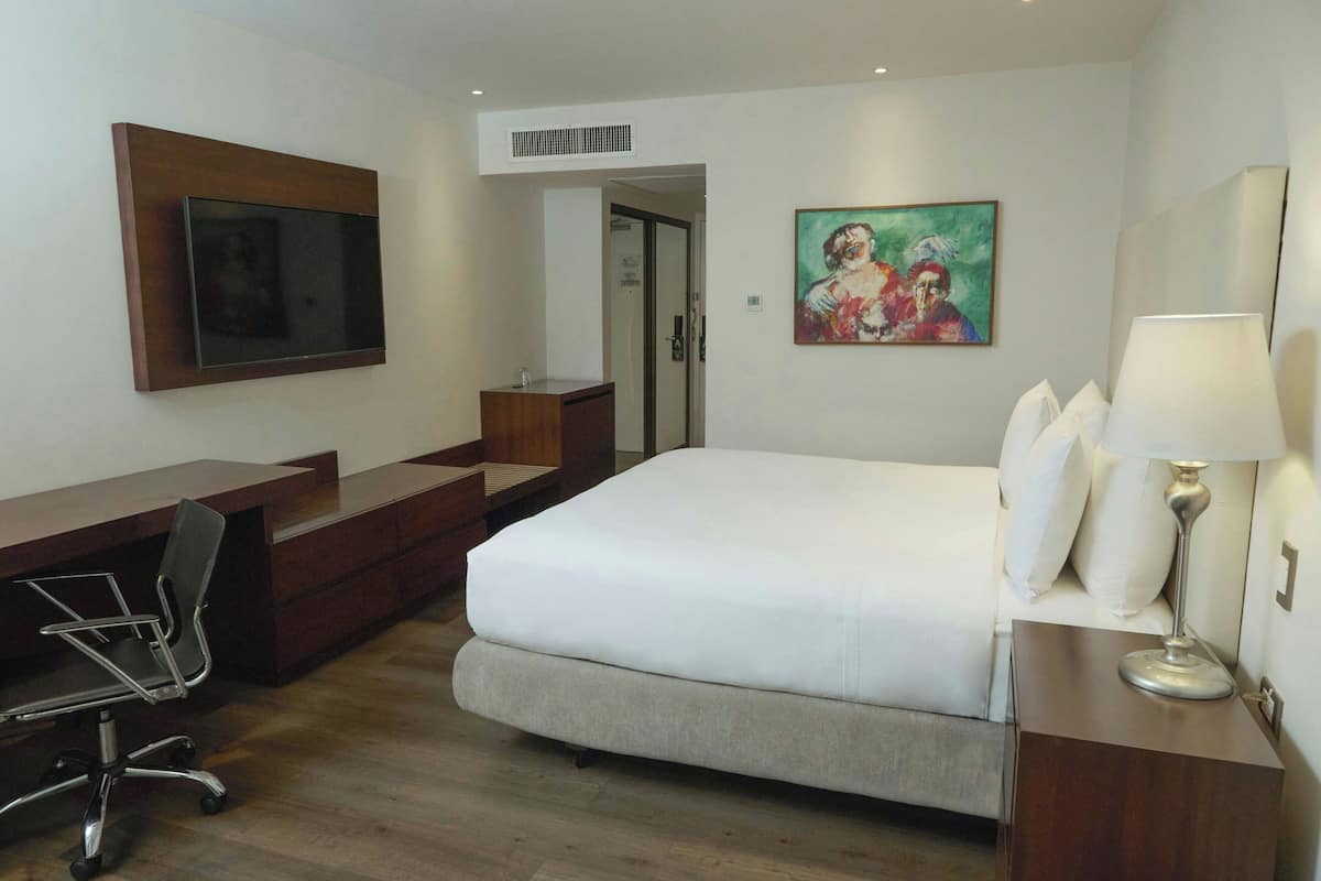 A hotel room with a bed, desk, chair, and artwork on the walls.