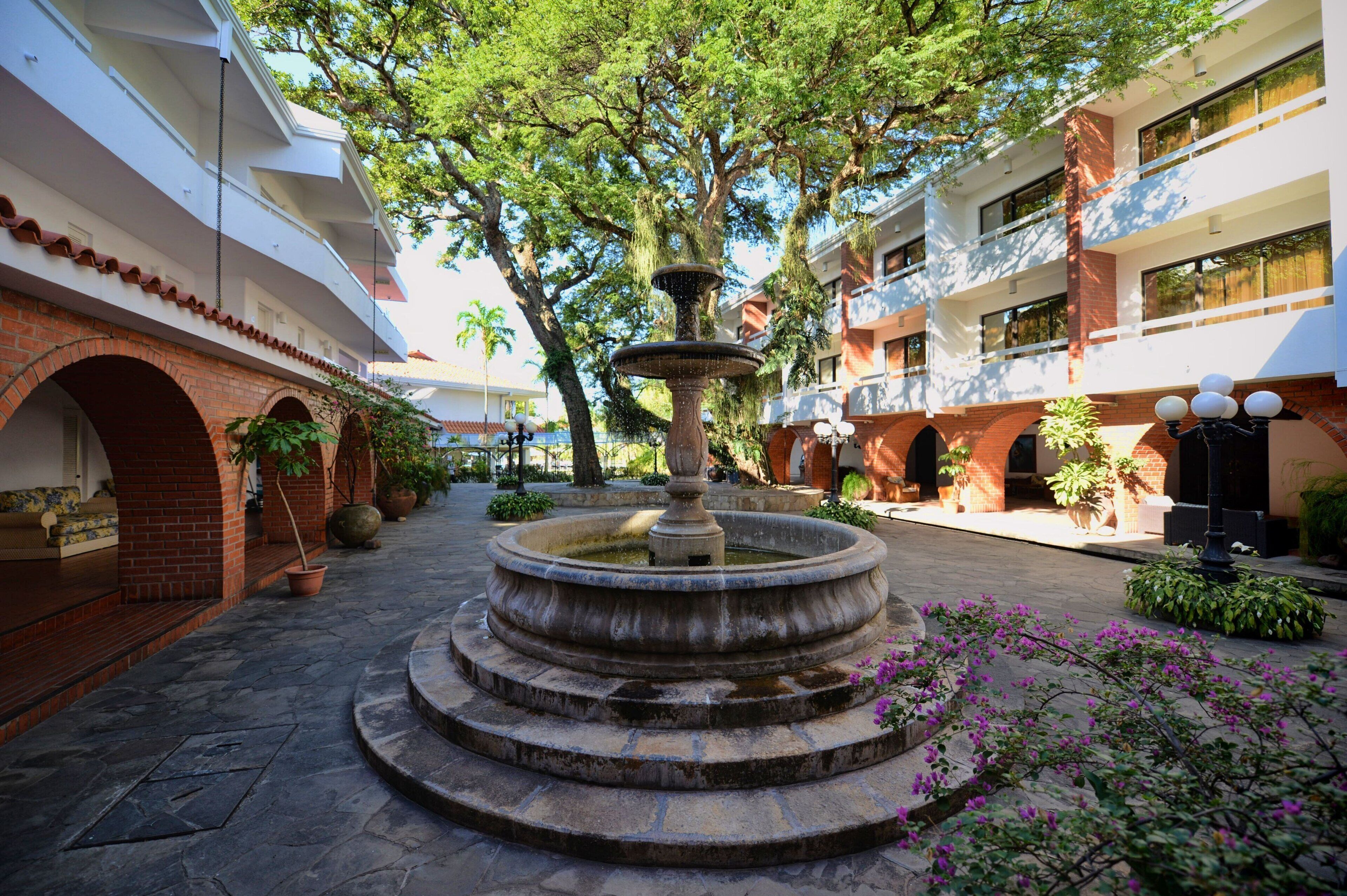 Un patio con una fuente central, rodeado de arcos de ladrillo y plantas en macetas.