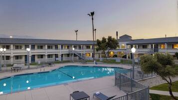 A hotel with a swimming pool, outdoor seating, and a well-lit building facade.