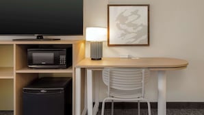 A compact hotel room with a flat-screen TV, a microwave, a small fridge, a table with a chair, and a framed artwork on the wall. - Spark by Hilton Santa Nella on I-5 (Gustine)