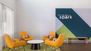 A modern room with four yellow rocking chairs around a central table, a wooden bench, and a geometric-patterned wall with a motivational quote. - Spark by Hilton Santa Nella on I-5 (Gustine)