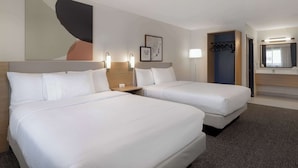 A hotel room with two beds, a large abstract painting, a framed picture, a coat rack, and a bathroom with a mirror and sink. - Spark by Hilton Santa Nella on I-5 (Gustine)