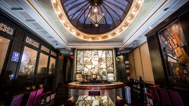 A bar area with a high ceiling, a central chandelier, and a bar counter with stools. - The Mansfield Hotel (New York)