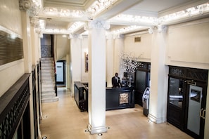 A grand lobby with a marble staircase, a reception desk, and a fireplace.