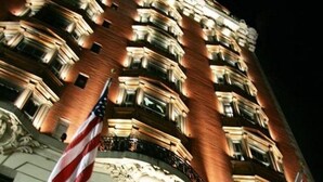 A grand hotel with a prominent American flag, ornate architectural details, and a series of balconies. - The Mansfield Hotel (New York)