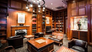 A library with wooden bookshelves, leather chairs, a fireplace, and a chess table. - The Mansfield Hotel (New York)