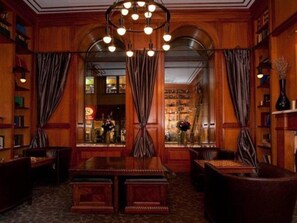 A warmly lit library with wooden bookshelves, a central table, and a chandelier. - The Mansfield Hotel (New York)