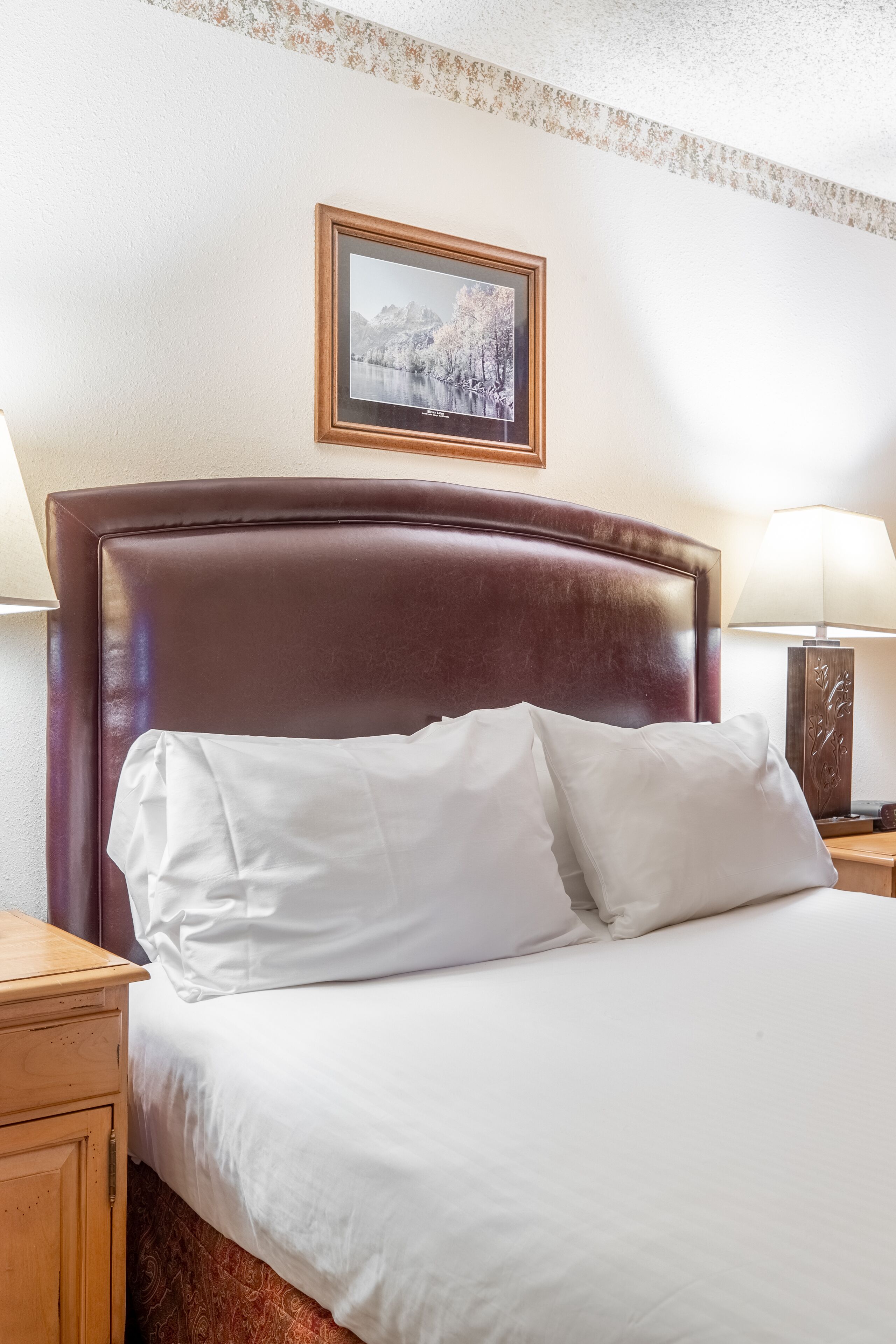 Cama bem arrumada com lençóis brancos e cabeceira de madeira.
