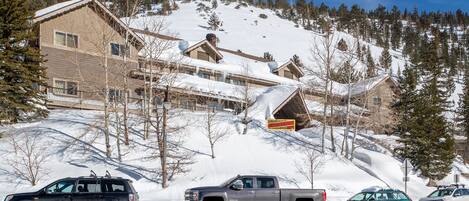 Una montaña nevada con un albergue y una carretera con vehículos estacionados.