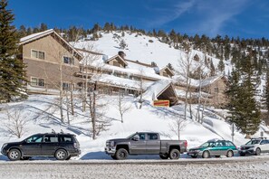 A snow-covered mountain with a lodge and a road with parked vehicles.