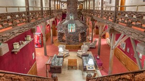 A high-ceilinged hall with a central stone fireplace, wooden railings, and a red carpeted floor. - Heidelberg Inn (June Lake)