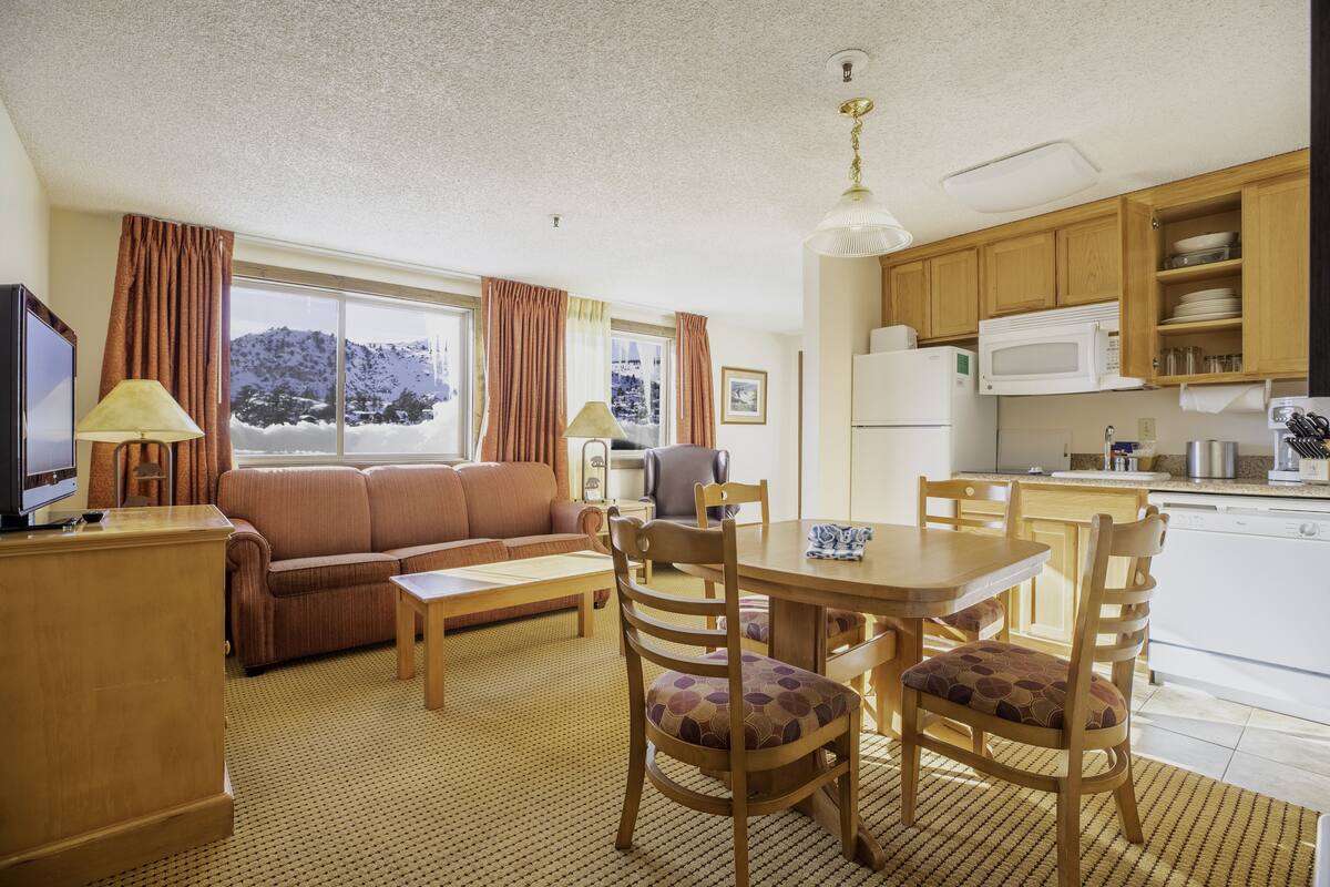 Ein gemütliches Wohnzimmer mit einer Couch, einem Fernseher und einem Essbereich mit Stühlen und einem Tisch.