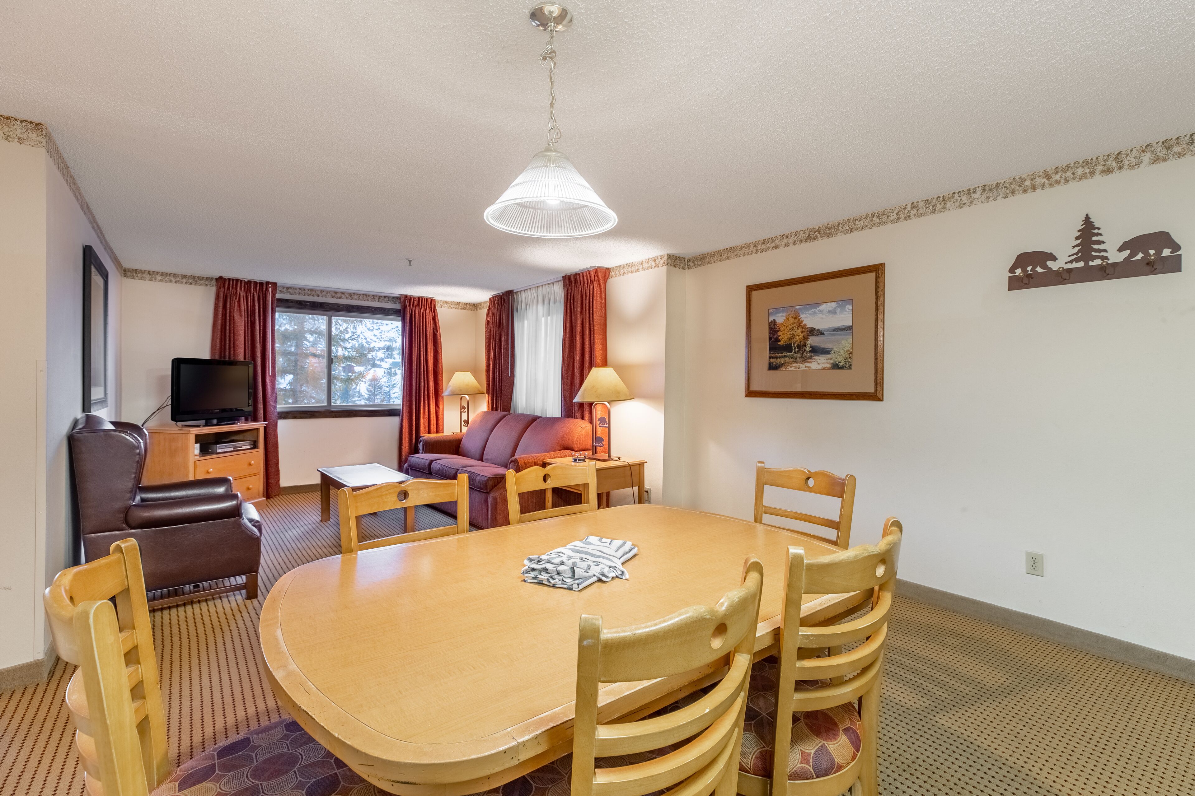 Een kamer met een houten eettafel, stoelen, een bank, een televisie en een lamp.