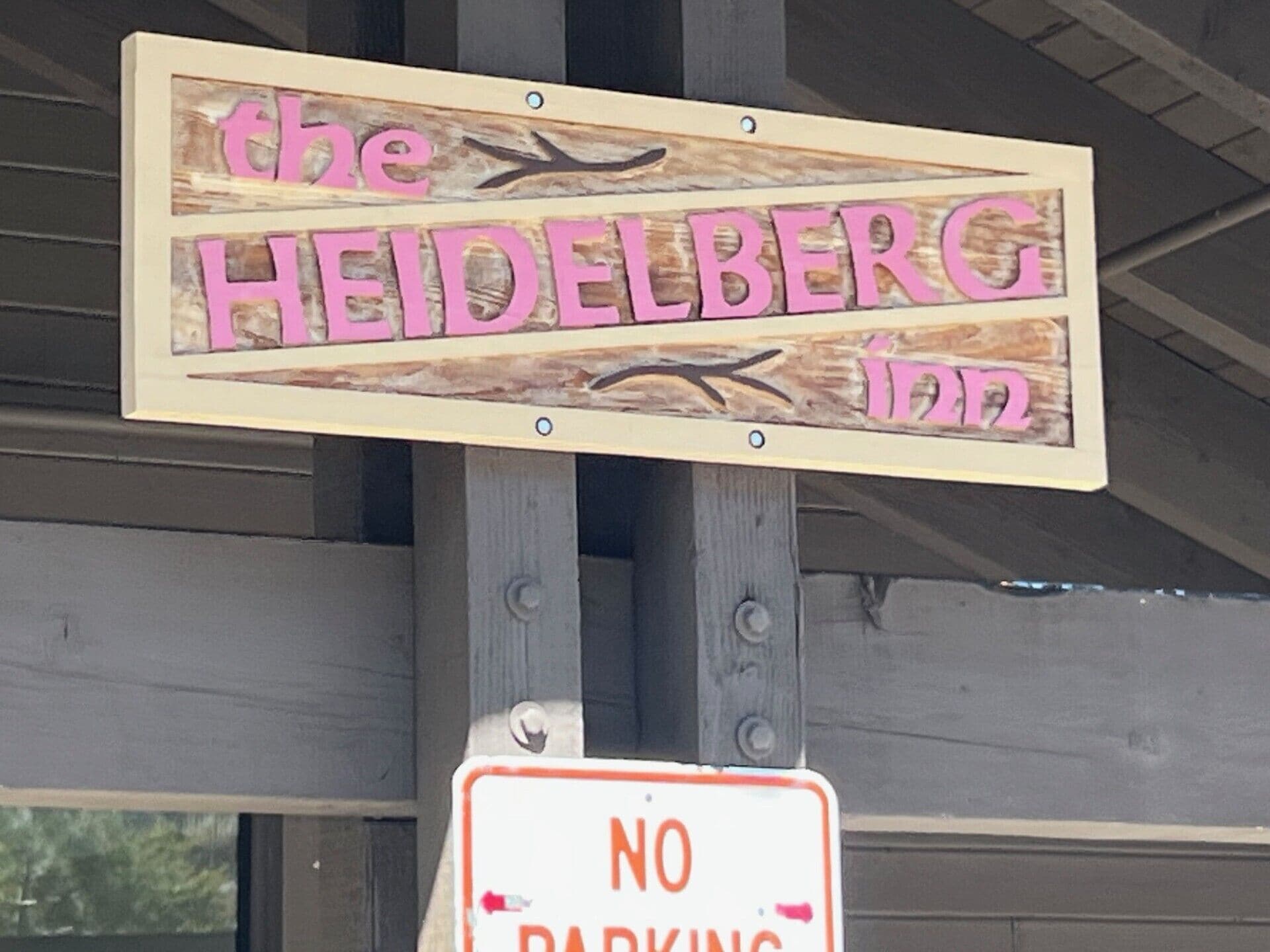 Een houten bord met de tekst 'The Heidelberg Inn', met daaronder een bord waarop 'GEEN PARKEOREN' staat.