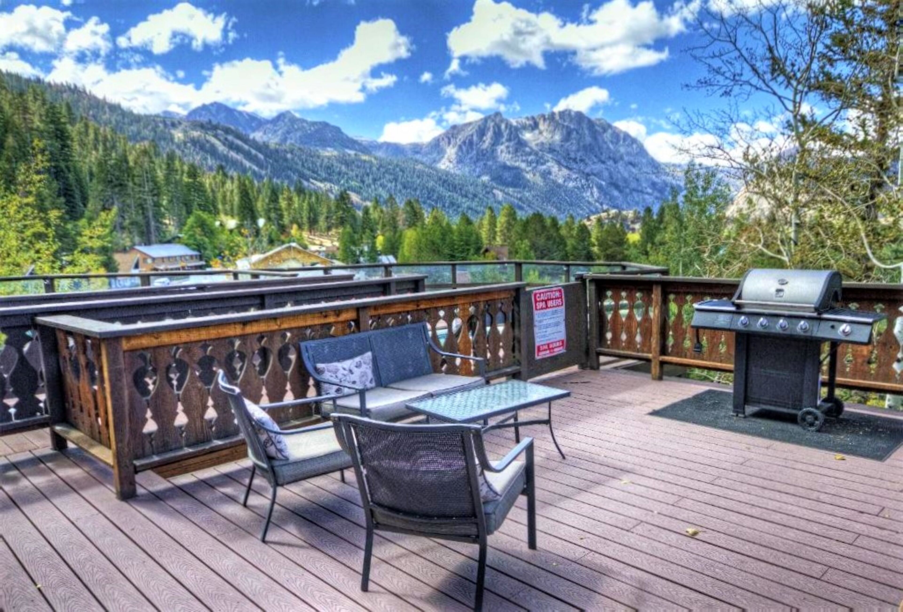 Une terrasse avec coin salon extérieur, un barbecue et une vue sur les montagnes.