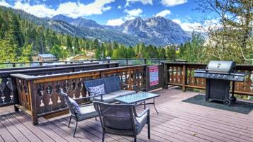 Une terrasse avec coin salon extérieur, un barbecue et une vue sur les montagnes.