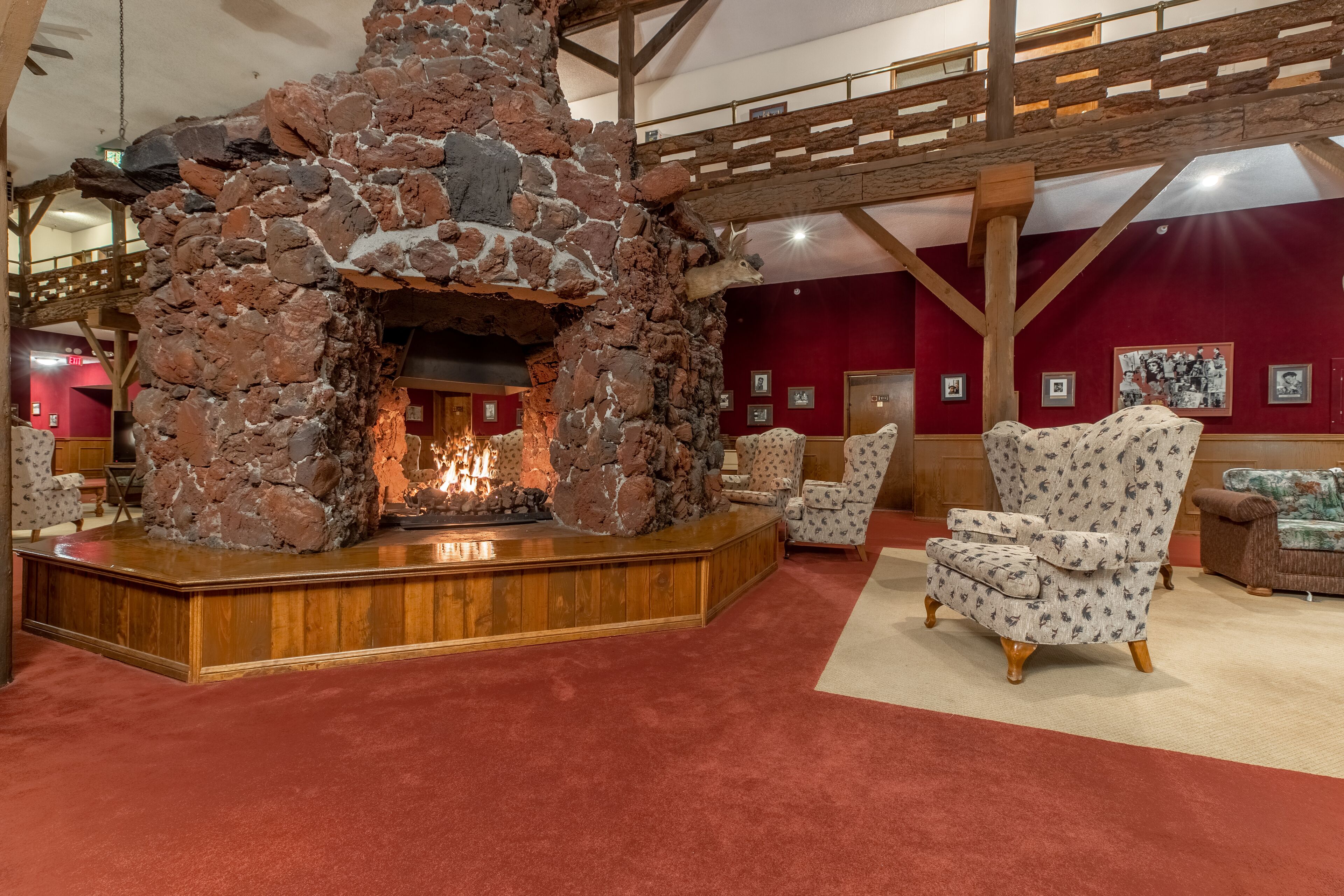 A stone fireplace with a fire, surrounded by patterned chairs and a wooden bench.
