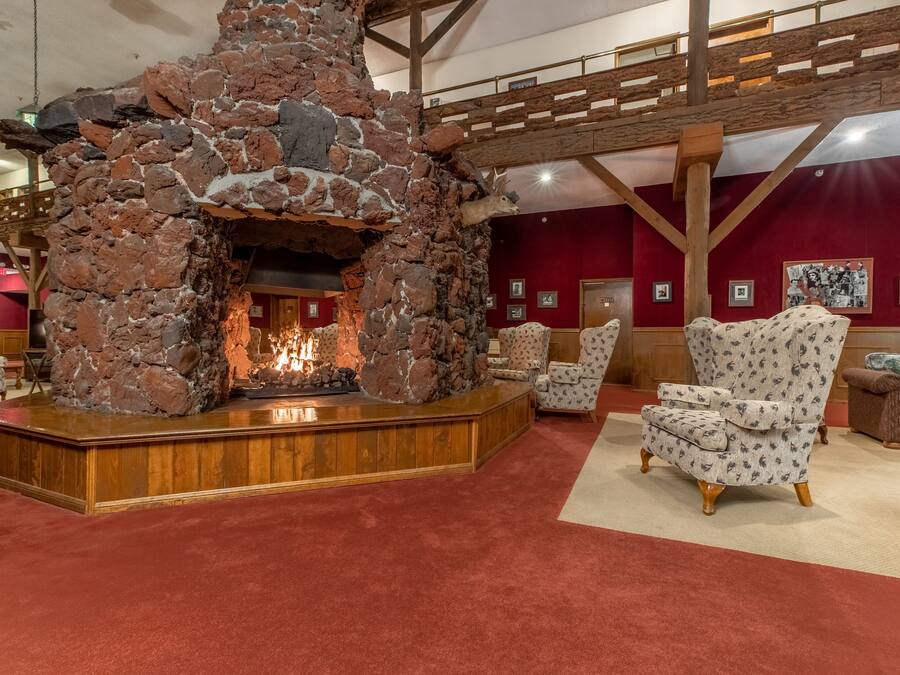 Una chimenea de piedra con fuego, rodeada de sillones estampados y un banco de madera.