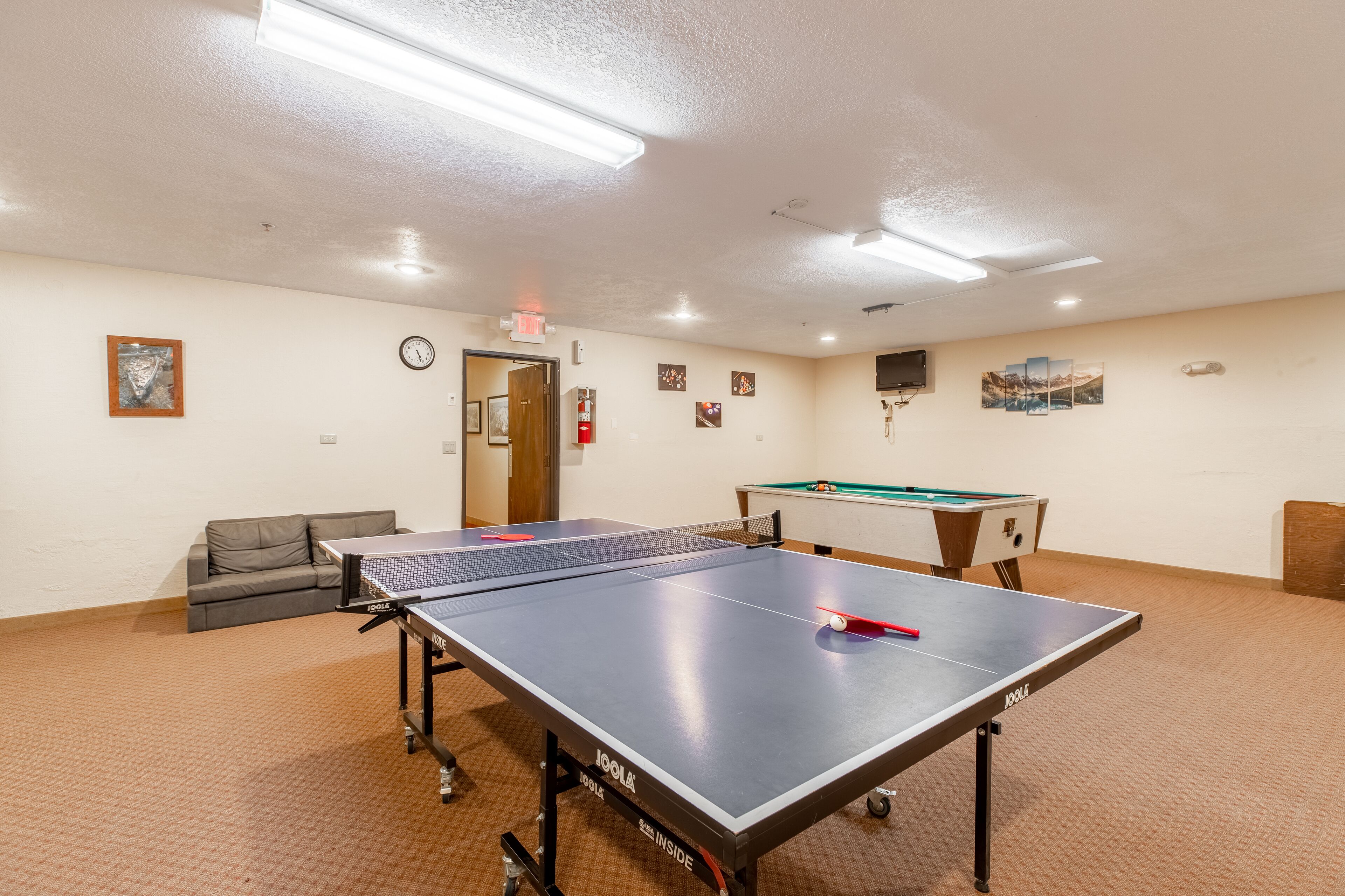 A room with a ping pong table, a pool table, a sofa, and a clock on the wall.