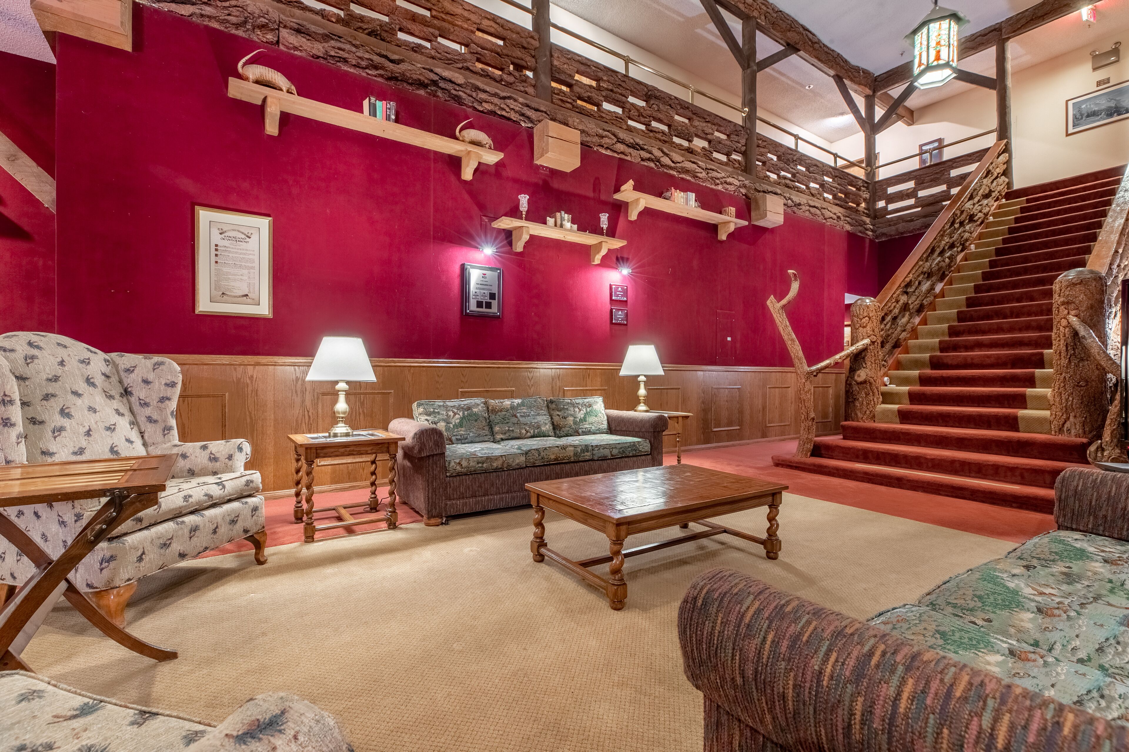 A lobby with a red wall, wooden furniture, a staircase, and a chandelier.
