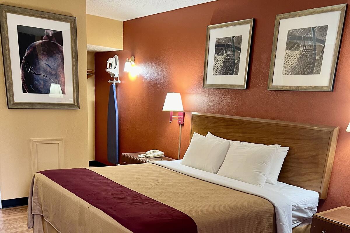 A hotel room with a large bed, a nightstand, a lamp, and framed pictures on the wall.