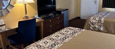 Habitación de hotel con dos camas, un escritorio con televisor, una silla, un aparador y una puerta.