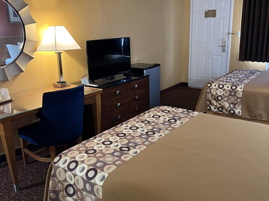A hotel room with two beds, a desk with a TV, a chair, a dresser, and a door.