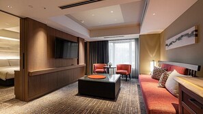 Een hotelkamer met een bank, een salontafel, een aan de muur bevestigde televisie en een raam met gordijnen.