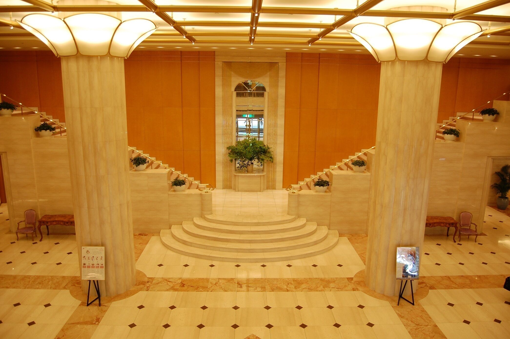 A grand lobby with marble flooring, a central staircase, and large columns.