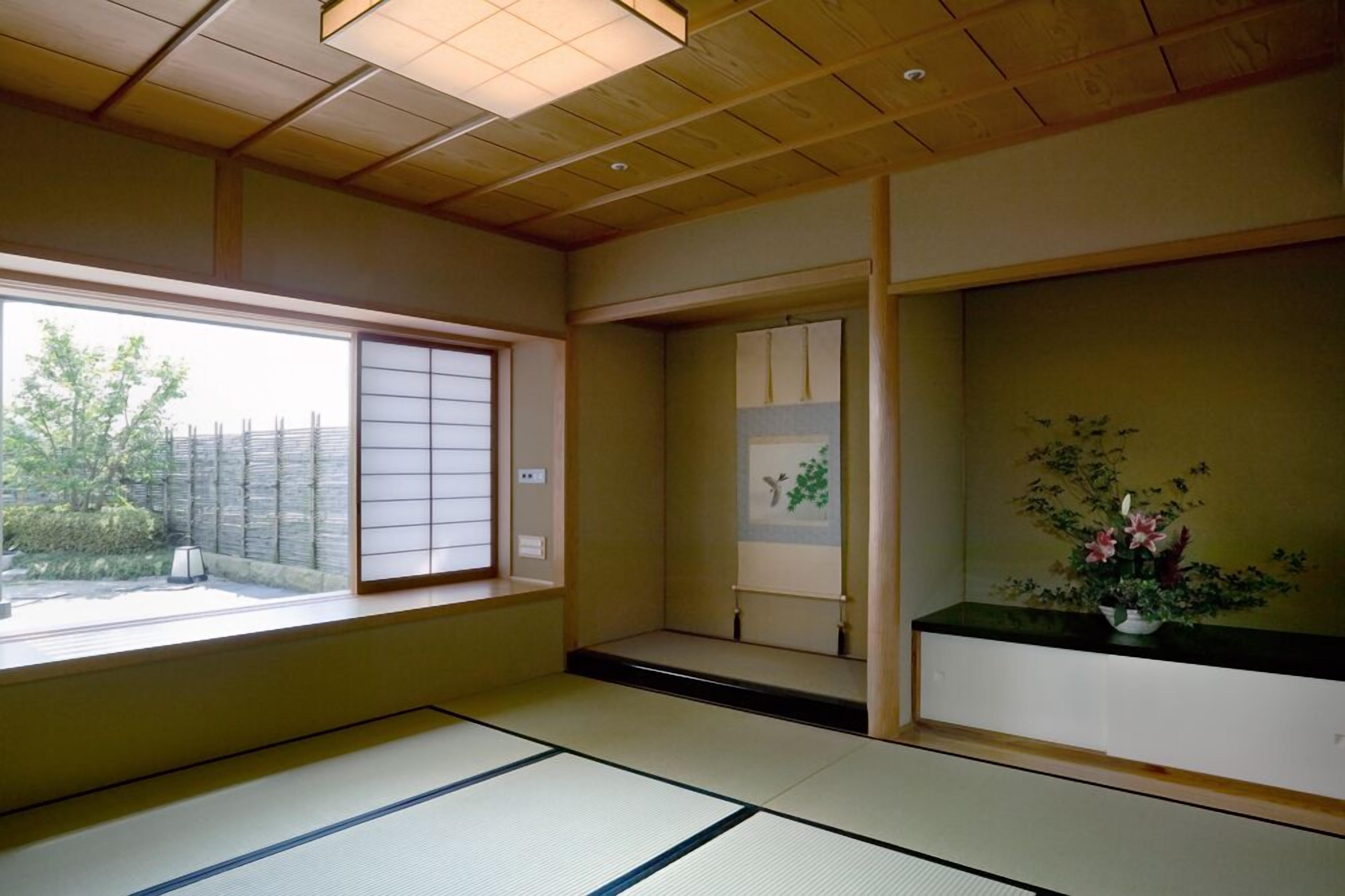 Una habitación japonesa tradicional con suelo de tatami, una puerta corredera shoji y vistas a un jardín.
