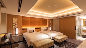 A hotel room with two beds, a desk, a chair, a small table, and a glass-enclosed shower area. - Hotel Nikko Fukuoka (Fukuoka)