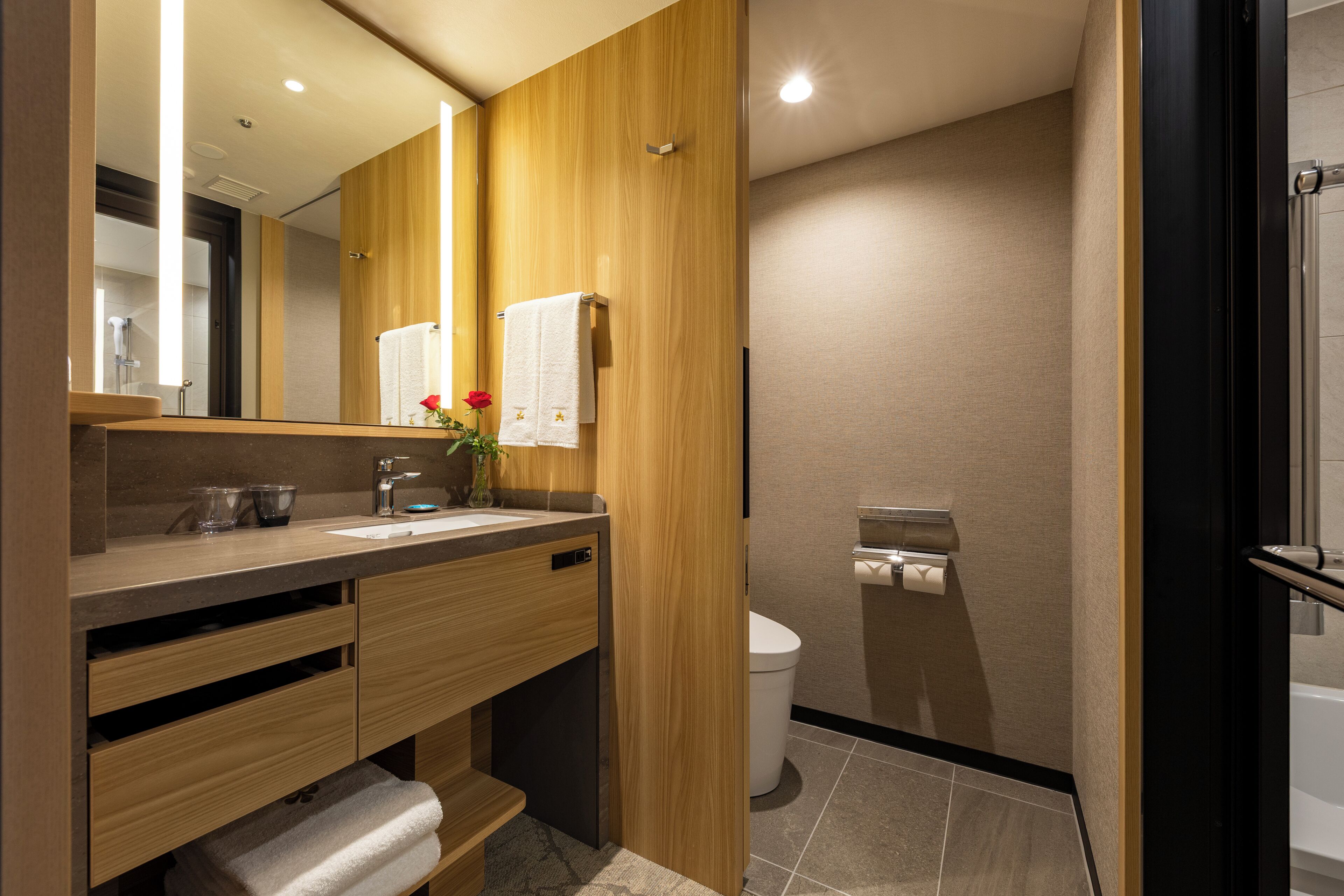 Un baño moderno con muebles de madera, un espejo grande, un lavamanos y un inodoro.