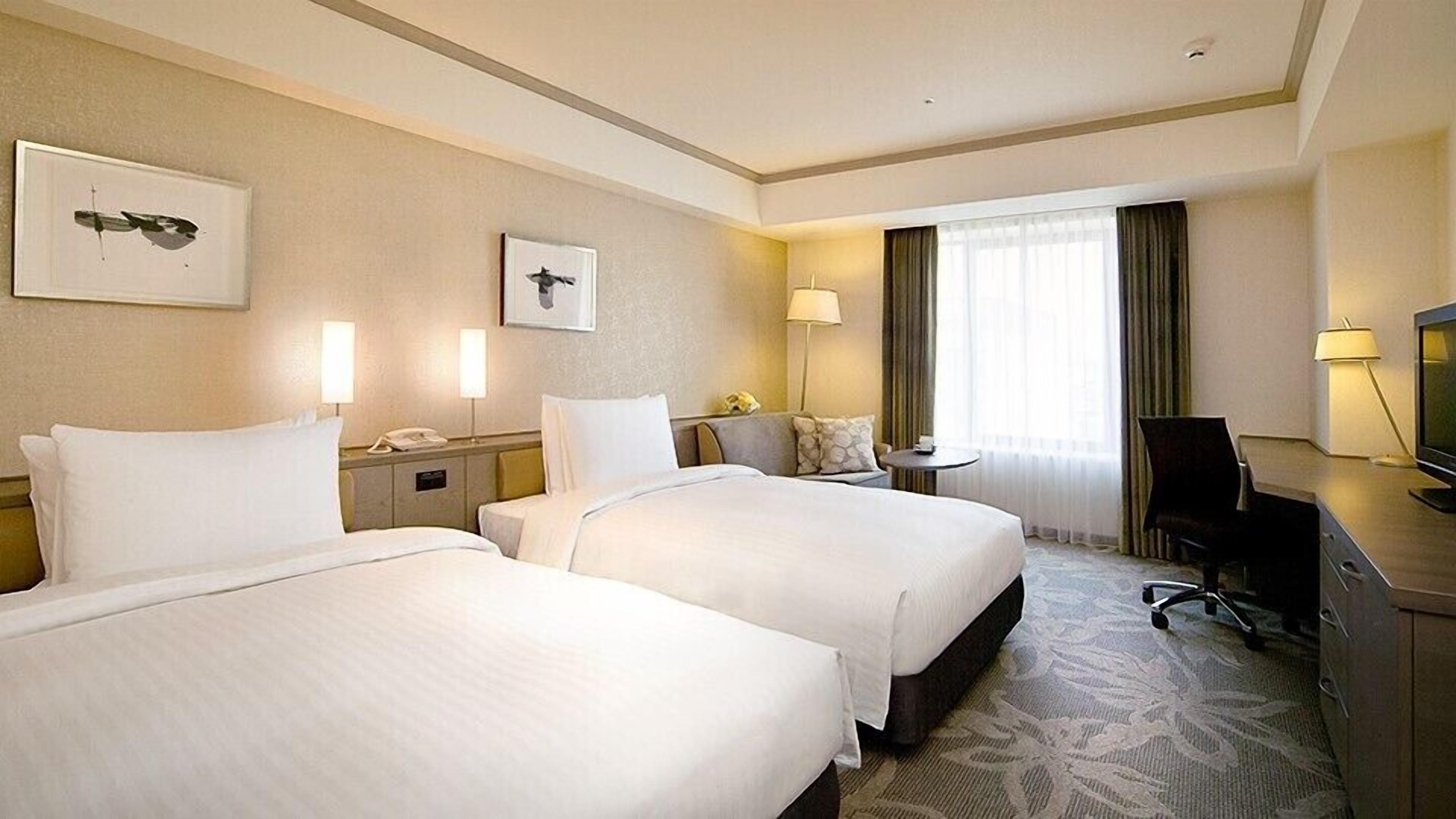 Ein Hotelzimmer mit zwei Betten, einem Schreibtisch, einem Sessel, einem Fernseher und Bildern an den Wänden.
