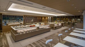 A modern dining area with a central buffet, multiple seating options, and a view of the kitchen in the background. - Hotel Nikko Fukuoka (Fukuoka)
