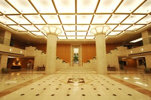 Een ruime lobby met een hoge plafond, brede zuilen en een centrale trap.